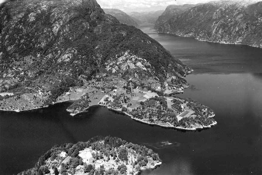 Olsnes 1960. Gamletunet midt på biletet, på oppsida av bygdevegen. Lengst til venstre bnr. 3 Klyvvikjæ. Mellom Klyvvikjæ og gamletunet ligg bnr. 4 Dalen. Bnr. 6 Tonjen lengst til høgre. Attom Tonjen ser ein bnr. 5 Kråkhaugen. I framgrunnen Ulvsnesøy. I bakgrunnen på andre sida av fjorden Fossmark. Foto: Widerøe’s Flyveselskap A/S.