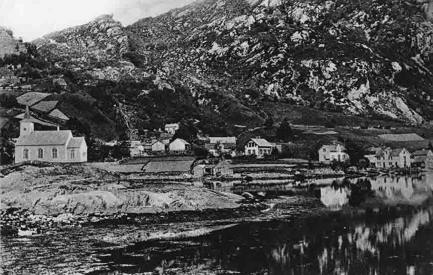 Bruvik 1905. Til høgre for kyrkja gamletunet på Kyrkje-Bruvik. Grensa mellom Kyrkje-Bruvik og Indre-Bruvik går til venstre for nausta. Attom nausta ligg husa på Bakken (bnr. 4-8 og 10).  Gamalt prospektkort. 